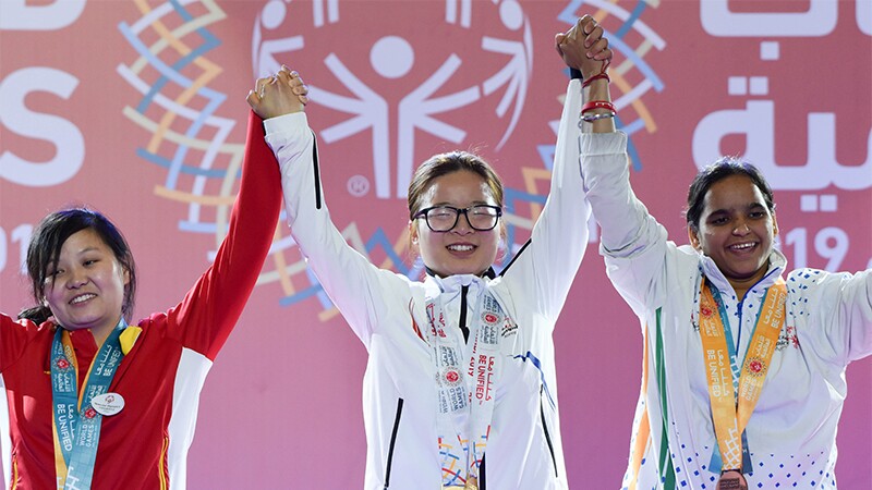 Three athletes at a medaling ceremony holding hands up in the air as a sign of victory. 