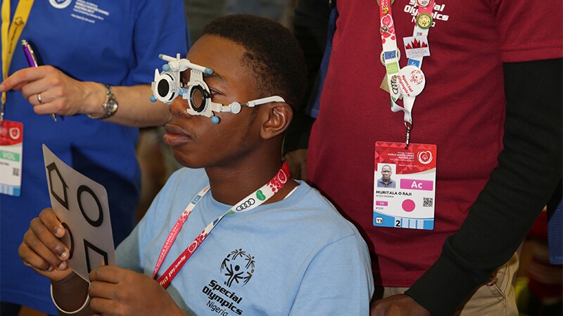 Athlete from Nigeria receiving an eye exam as observers look on.