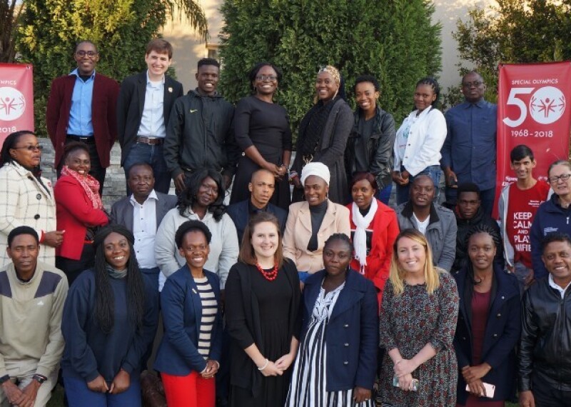 Participants from the Africa Region and Special Olympics International representatives pose for a group photo. Special Olympics 50th anniversary banners stand on either side of the groups back row. 