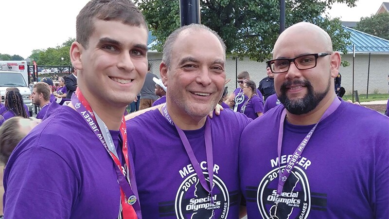 Coach Robert with his two sons Roberto Jr. and Coach Carlos; all three men wearing a MERCER 2019 Special Olympics New Jersey Games shirt.