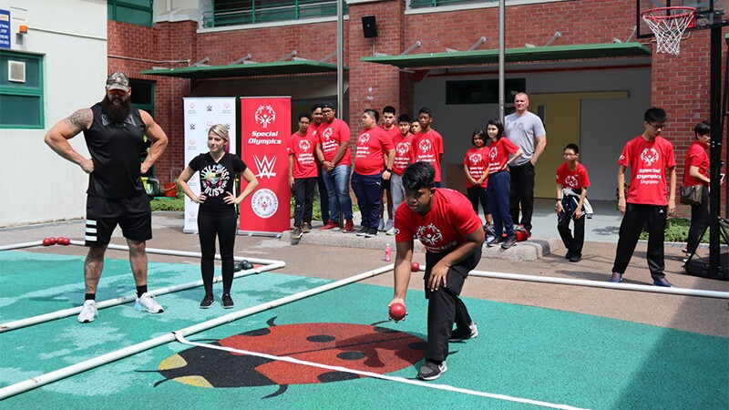 WWE pro stars and Singapore athletes play Bocce on a court outside.