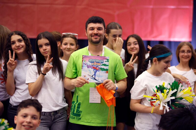 A man stands amid a crowd of young people holding up a children's book.