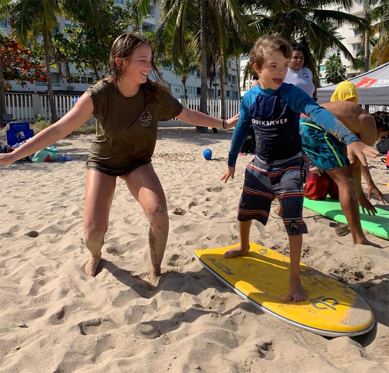 young athlete practicing on a surfboard in the sand as an adult show him how to surf.