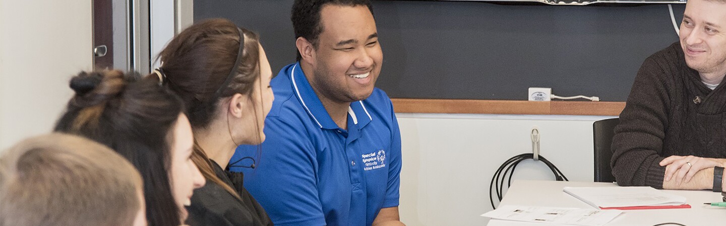 Young adults sitting at a table smiling and having a conversation.