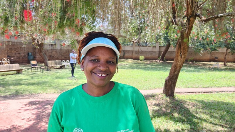 Margaret Gichuki smiles at the camera while standing in a grassy area with trees.