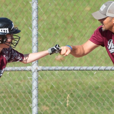 Female baseball player fist-bumping a coach.