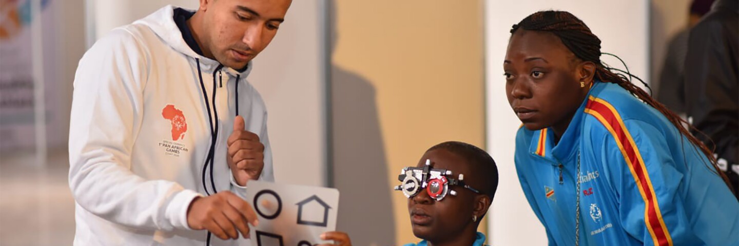Athlete being given an eye exam by a volunteer and an observer watching.