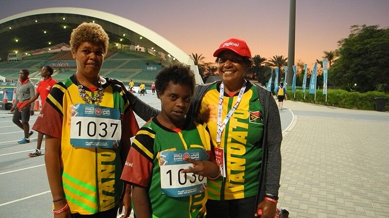 Two athletes and a coach stand in front of the stadium in Abu Dhabi.