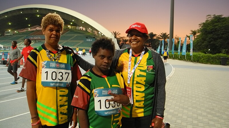 Two athletes and a coach stand in front of the stadium in Abu Dhabi. 