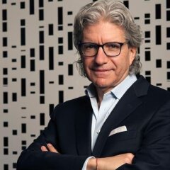 David Sable with his arms cross in a navy blue suite in front of a black and white wall.