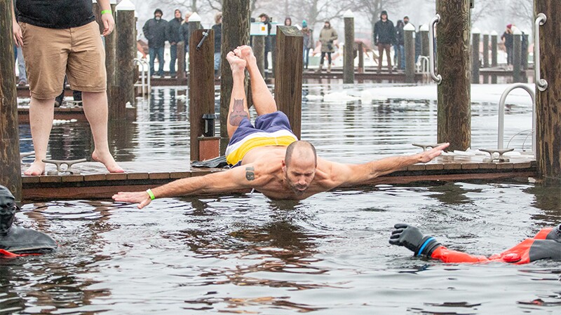 Man jumping off a dock and doing a belly flop as onlookers watch.