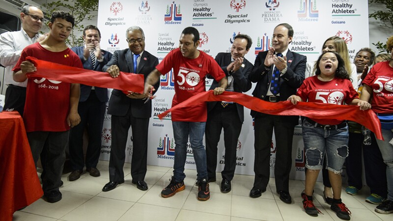 Athletes and representatives cut a ribbon in front of a Healthy Athletes backdrop.