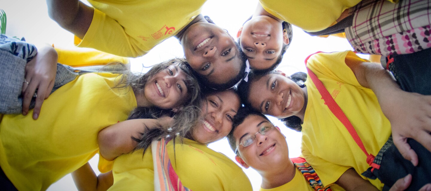 Children wearing yellow t-shirts standing in a circle smiling as they look down at the camera