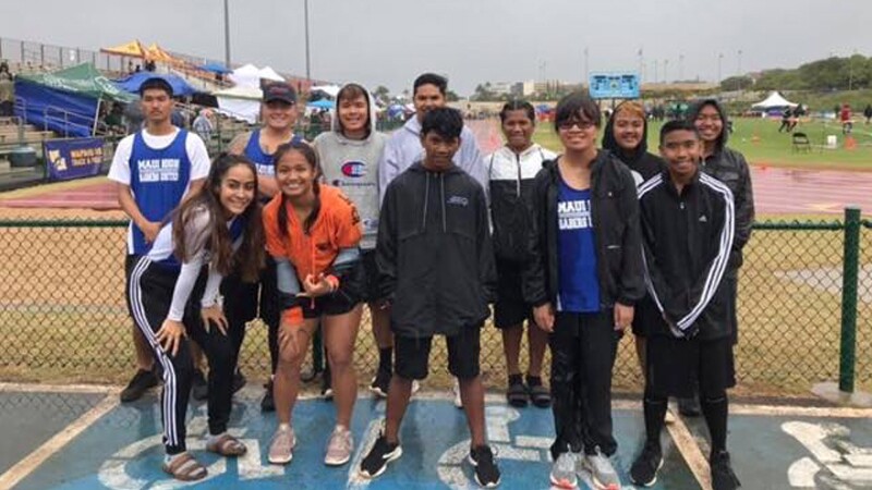 Group of young individuals standing for a group photo in front of a fence on a field.