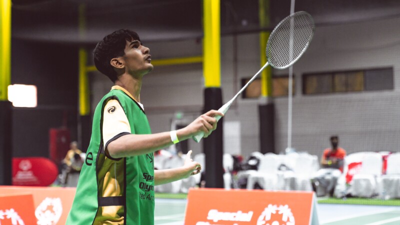 An athlete standing on the badminton court with racket in the air looking towards where the Shuttlecock is expected to come over the net