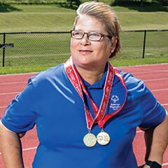 Maryann Gonzales standing in front of a track and field with awards draped around her neck.