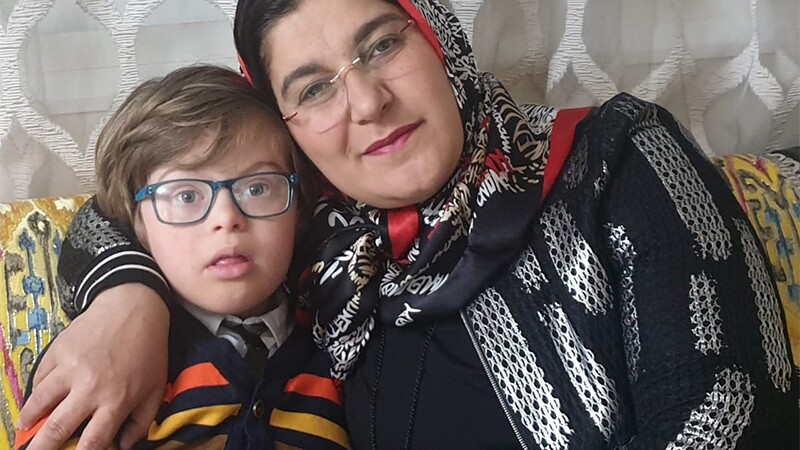 A mother with her arm around her young son, leaning against him and smiling.