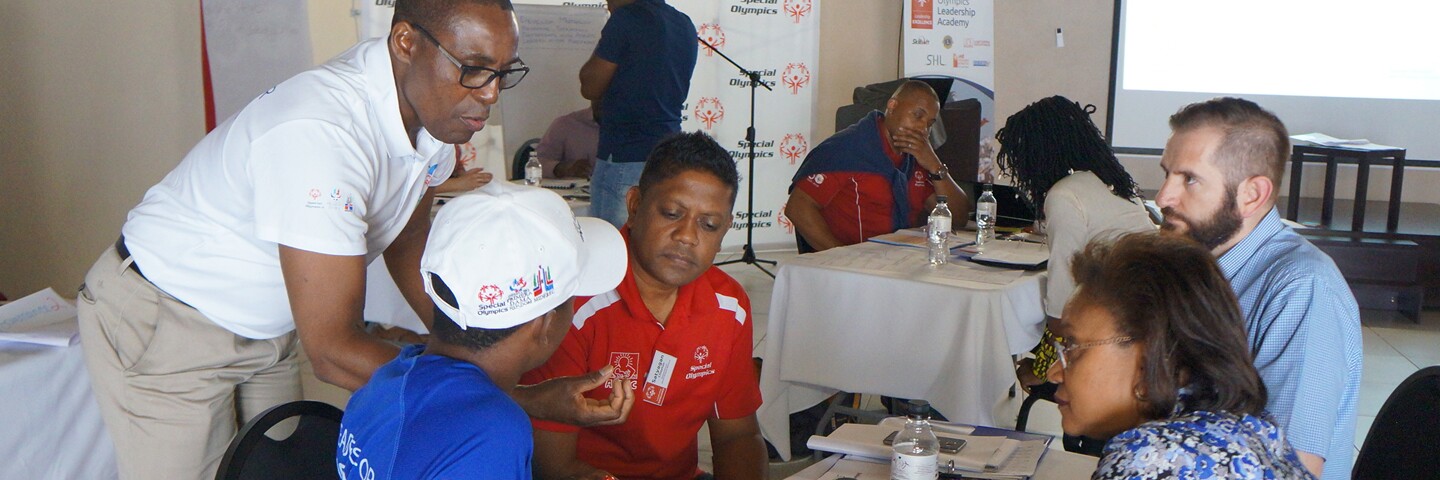 Athletes and Special Olympics representatives sitting around a table conversing. 