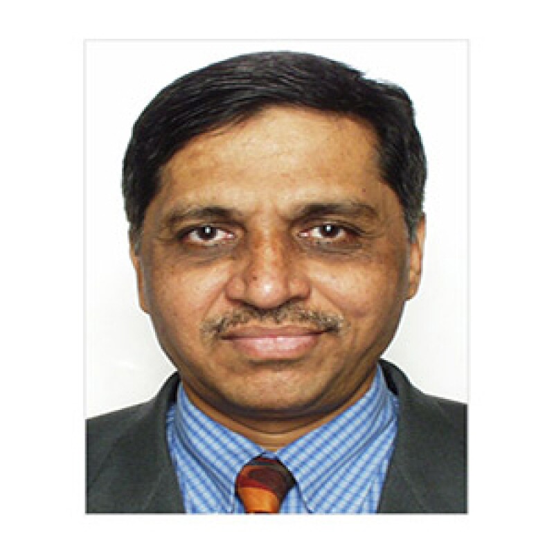 Dr. Asoke Dhoble in a dark suite and blue shirt with gold tie.