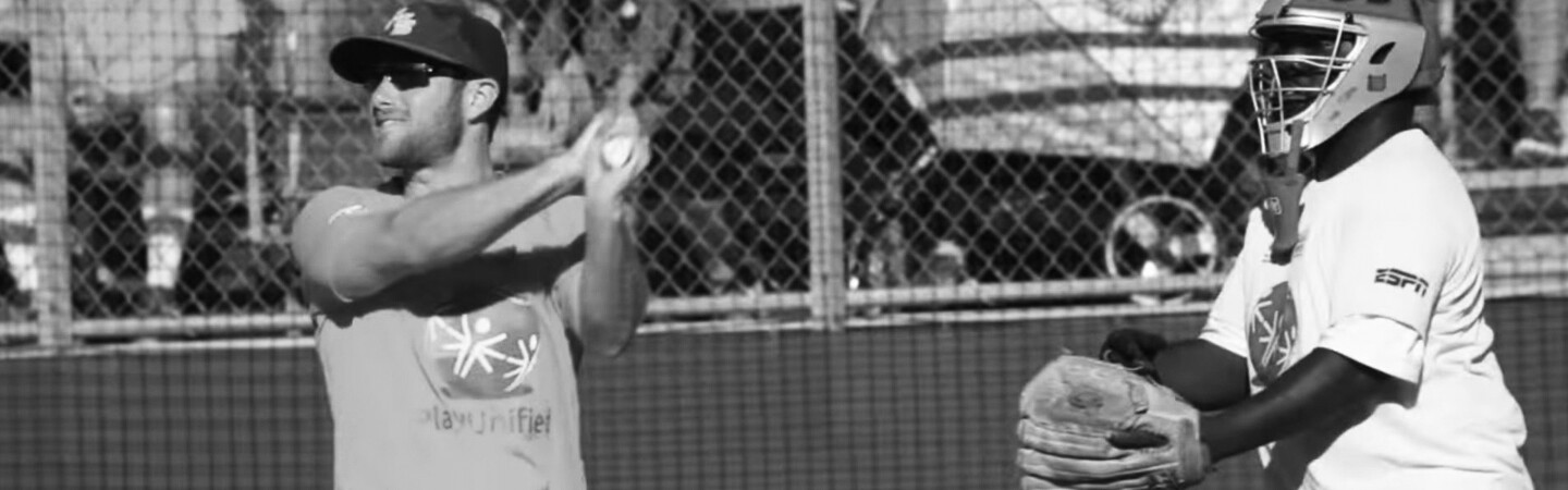 man in a play unified t-shirt hitting a ball as the catcher prepares to catch it.