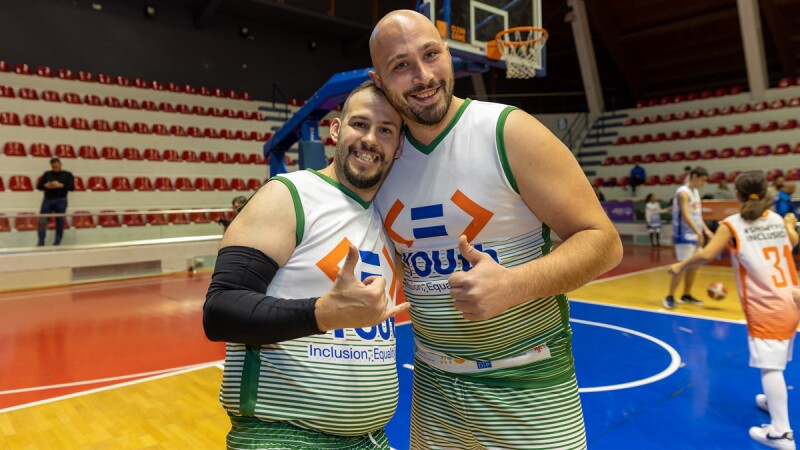 Two men wearing basketball jerseys on a basketball court posing and smiling at the camera
