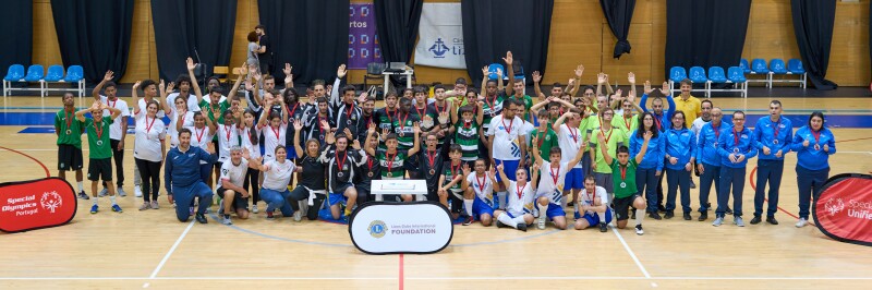 A group shot of football teams. In front of them, a table with a cake on it.