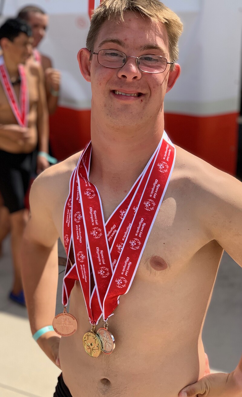 Chris Nikic standing after a swim meet with medals round his neck.