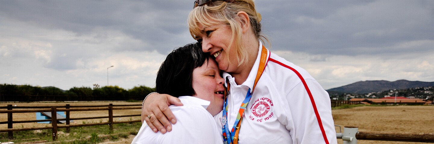 Volunteer hugging an athlete outside with a field in the background.