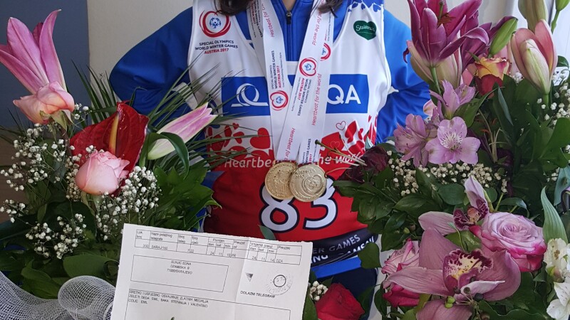 Mujer joven de pie con sus medallas alrededor de su cuello y flores a su alrededor.