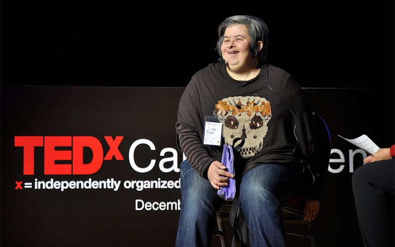 Dina Galal sitting on a chair in front of the TEDx signage at her TEDx presentation