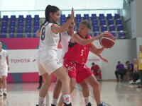 A group of three young girls playing basketball. Two girls wearing white jersey man-marking the third one who is holding the basketball and wearing the red uniform of the opposite team.