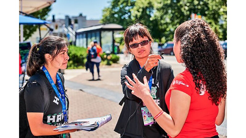 Two young women use a microphone to interview another woman.