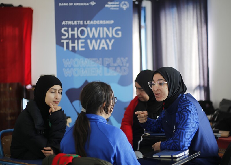 Three young women sitting at a round table talking. 