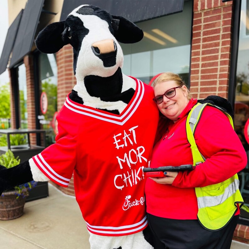 Menina em pé com o mascote Chick-fil-A. 