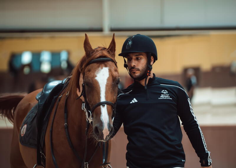 a man in an equestrian outfit standing next to a horse and holding the reins. 