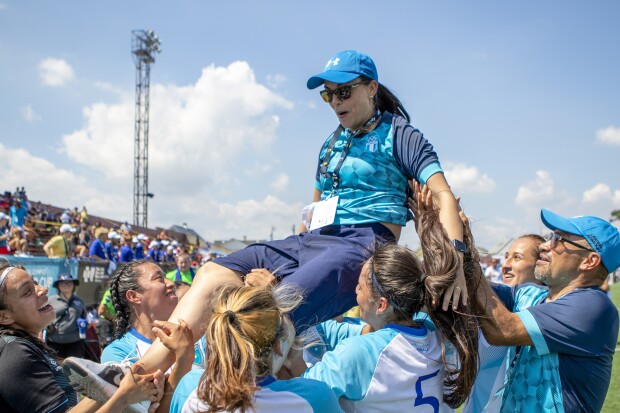 Coach being lifted up by athletes on the field.