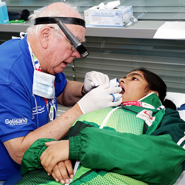 Female athlete dressed in green laying back and a dentist examines her teeth.
