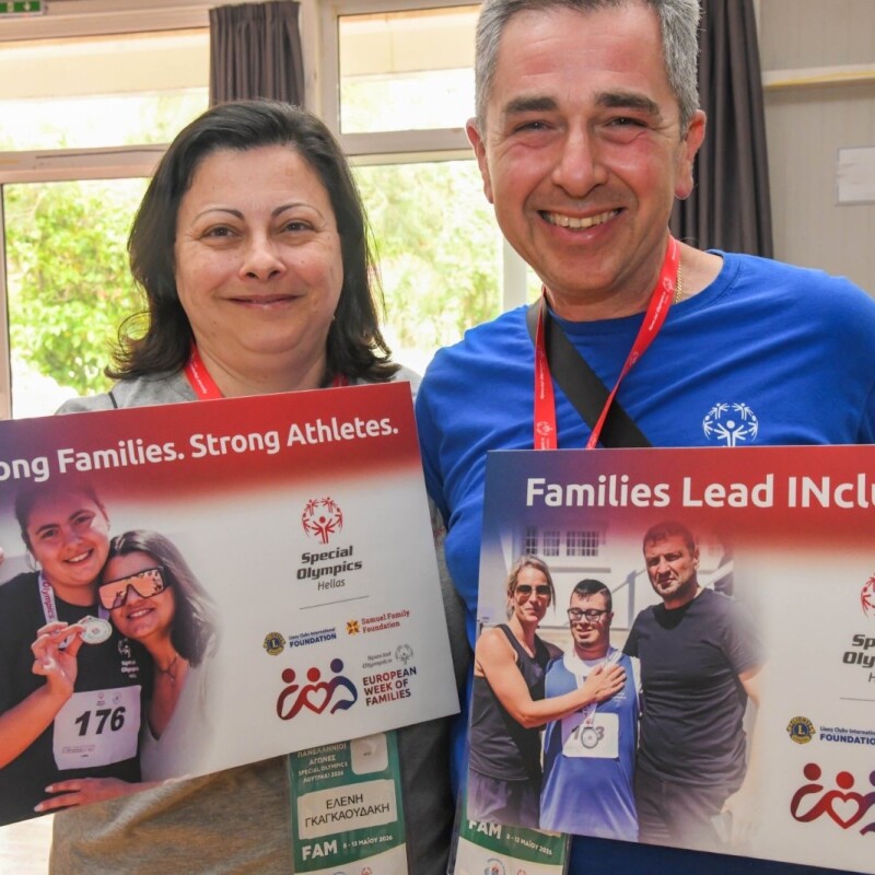A man and a woman stand together holding branded posters for Special Olympics European Week of Families. 