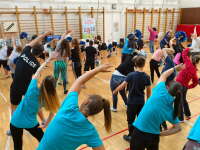 Participants in blue t-shirts all lean to their right with their arms overhead stretching.