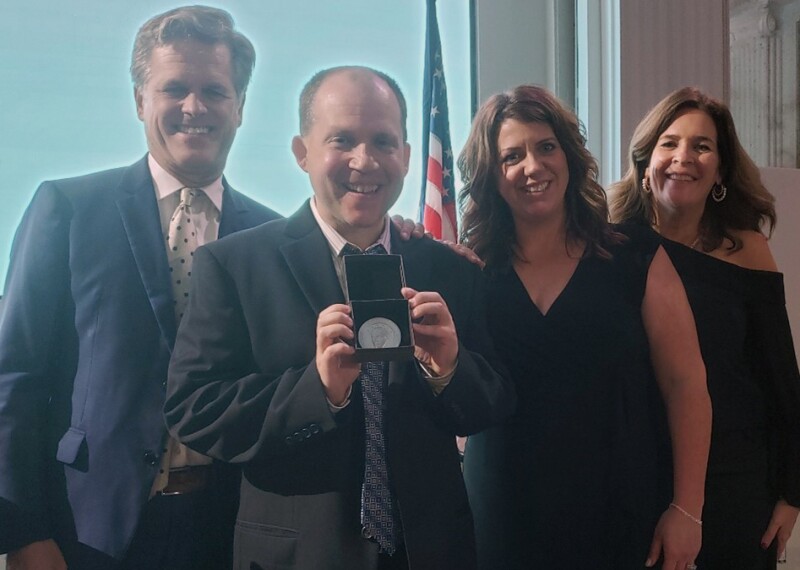 Four people side by side, a man is showing an award. 