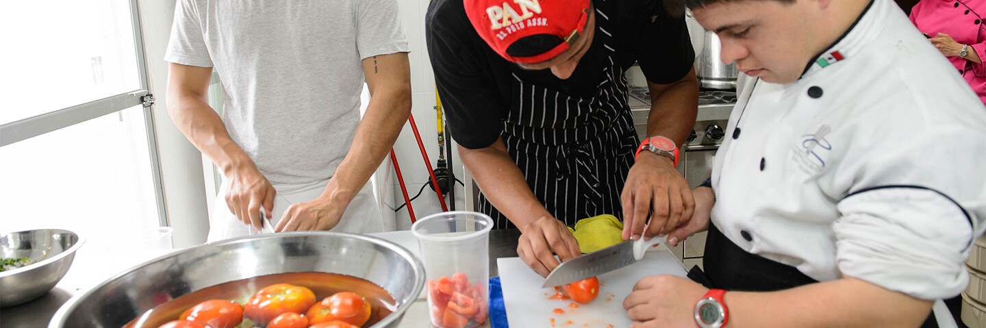 a chef showing an athlete how to cut a tomato.