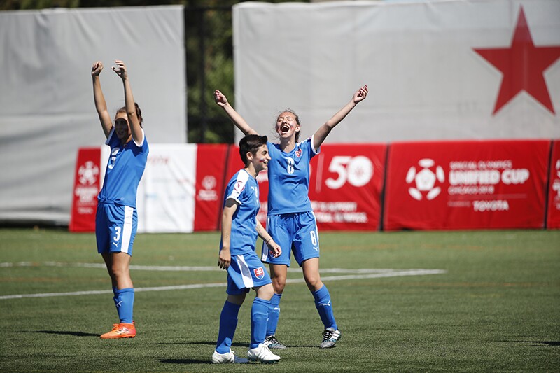 Three female football athletes on the field celebrating at the Unified Cup competition.