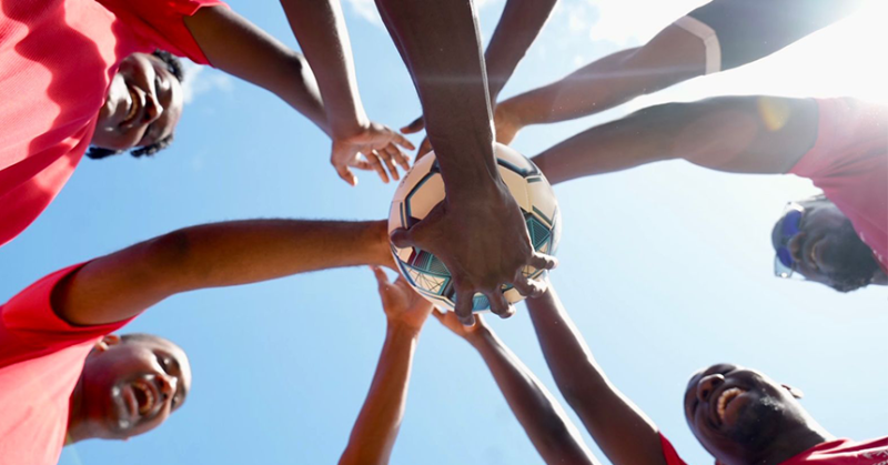 a group of athletes standing in a circle putting their hands in the middle, one on top of the other. 