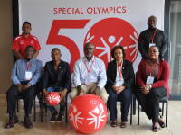 5 people sit and 2 people stand looking official in front of a Special Olympics 50th anniversary banner. 
