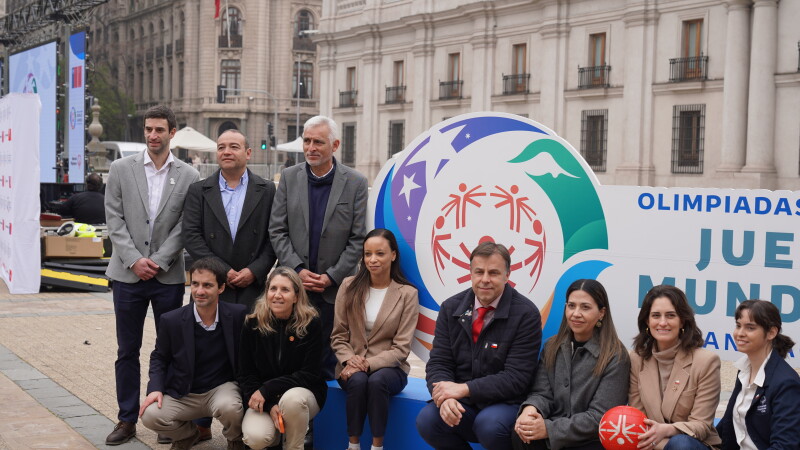 A group of 10 people in two rows in front of Santiago 2027 branded signage. 