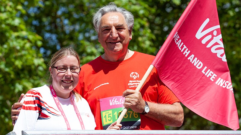 Lyn Dumbleton Special Olympics GB Athlete Leader standing with Jim Carter Actor (Downton Abbey) and Special Olympics GB Ambassador arm around her; both are holing a flag.
