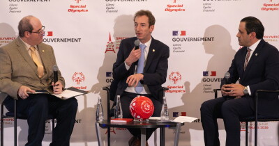 Three mean in a "panel" on stage. the man in the middle is speaking and the other two are listening. 