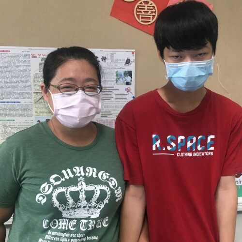 張明哲and his mother, 林芳怡, standing shoulder to shoulder posing for a picture with masks on