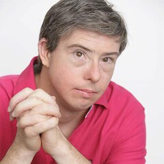 Eddie Barbanell in a red polo with his hands clasped in front of him looking at the photographer.