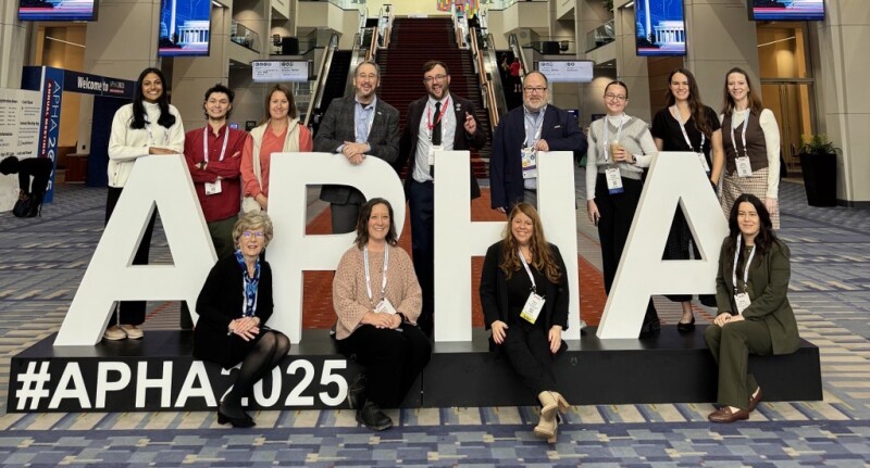 A large group of people pose around a sign titled “APHA.”